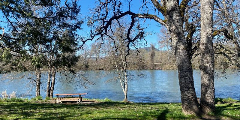 Picnic table by a river with trees and hills in the background.
