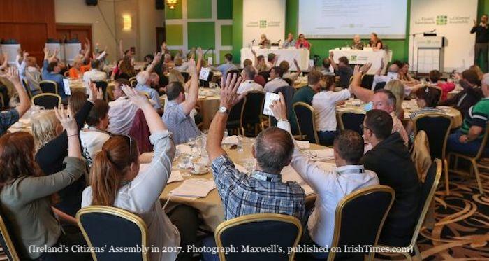People raising hands in a conference room with panel speakers at the front. Ireland's Citizens’ Assembly in 2017. Photograph: Maxwell's, published on IrishTimes.com