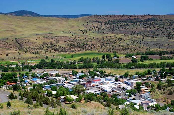 A small town surrounded by rolling, sparsely vegetated hills under a clear blue sky. Photo: Gary Halvorson, Oregon State Archives